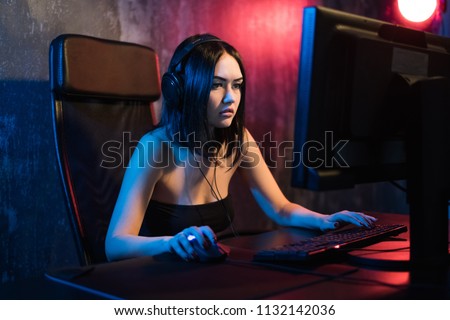 A cute female gamer girl sits in a cozy room behind a computer and plays games. Woman live streaming computer video games to her fans. Streamer and gamer concept