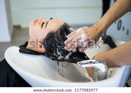 Unrecognizable professional hairdresser washing hair to her client. Beautiful hairdresser washing hair to her client lady in hairdressing saloon. Client sitting with her eyes closed.