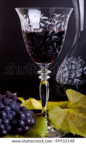 Old style wineglass and carafe with red wine, grapes and leaves on the foreground and dark background