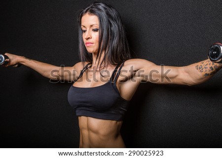 Muscular female bodybuilder exercising with dumbbell weights, black studio background.