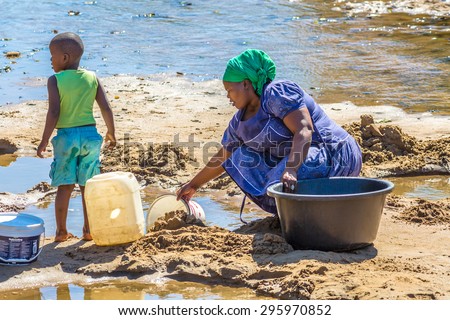 UMkhuze Game Reserve, South Africa - August 24, 2014: African woman with child collecting water from the river on the road leading to local Game Reserve.