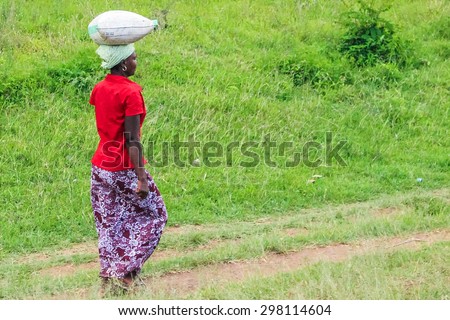 Arusha, Tanzania, Africa - January 12, 2013:  A young woman walks carrying an heavy bag on her head for a long distance to home.