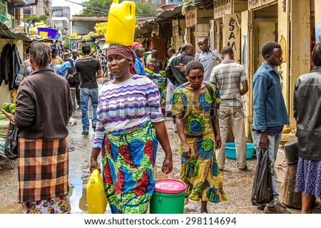 Arusha, Tanzania - January 2, 2013: A woman walks on her head carrying a yellow tank  in a market of the town