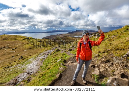 Smiling young woman takes a selfie during the trekking to The Old Man of Storr near Portree, Isle of Skye, Scotland, United Kingdom.
