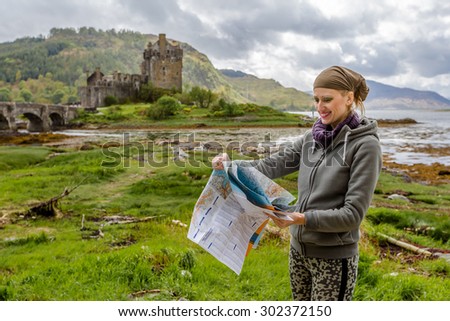 Young woman tourist looks at a road map. In background the famous and spectacular Eilean Donan Castle in Dornie, Kyle of Lochalsh, Scotland, United Kingdom.