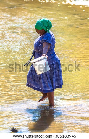 UMkhuze Game Reserve, South Africa - August 24, 2014: smiling african woman collecting water from the river on the road leading to local Game Reserve.