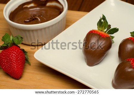 Freshly dipped chocolate covered strawberries on a white plate with chocolate bowl nearby