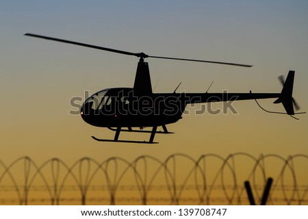 helicopter silhouette in flight over barbed wire fence