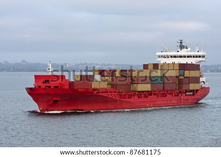 Container cargo ship in red, at sea.