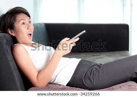 Young Asian Chinese/Japanese executive relaxing at home watching television on couch