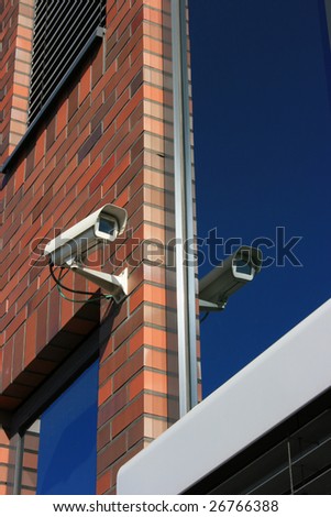security camera at brick wall and mirrored in window.