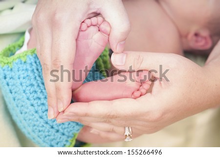 Little feet. Mother is holding newborn baby\'s feet in her hands that are shaped like heart