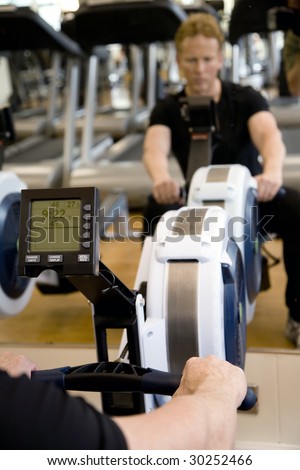 Close up of digital display on rowing machine in modern gym with reflection of personal trainer blurred in mirror.