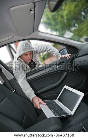 Car theft - a laptop being stolen through the window of an unoccupied car.  Shallow depth of field with focus on criminal.