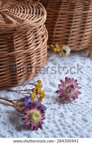 Wicker box of twigs and dried purple and yellow flowers on white vintage crochet Knitted napkin.