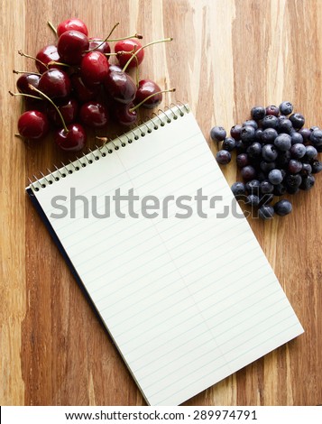 Steno spiral notebook with room for text or recipes on wood cutting board with fruits and berries
