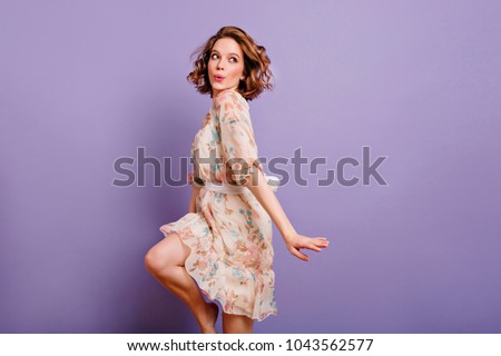 Inspired european young woman dancing in studio and laughing. Winsome brunette girl in cute dress jumping on purple background.