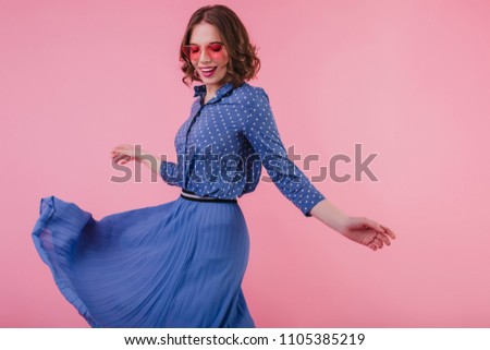 Wonderful european girl with tattoo dancing with inspired smile during studio photoshoot. Indoor portrait of attractive woman in long blue skirt.
