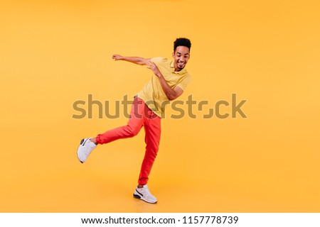Full-length portrait of joyful african male model dancing in yellow shoes. Cheerful black man enjoying photoshoot on bright background.