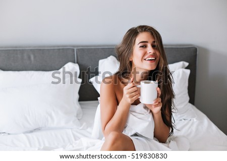 Portrait pretty girl with naughty shoulders drinking coffee on bed in the morning in apartment
