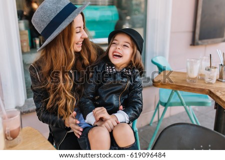 Portrait happy loving family, mother and daughter sitting in city cafe playing and hugging. Mother and daughter laugh sincerely. Styling family, true emotions, good day.