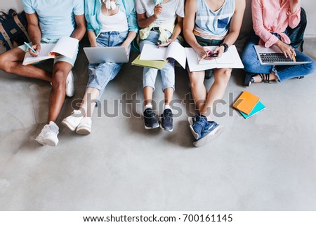 Overhead portrait of young people with laptops and smartphones, sitting together on the floor. Students writing lectures holding textbooks on their knees.