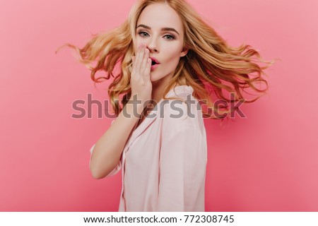 Dreamy white young woman with curly hair waving posing on pink background. Indoor photo of surprised caucasian lady in night-wear covering mouth with hand.