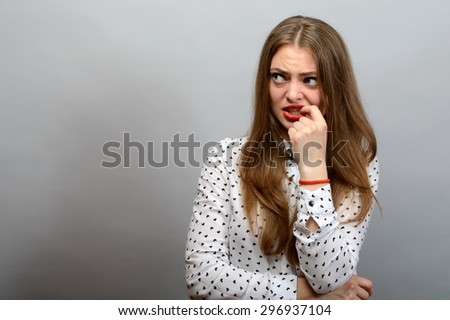 Cute woman thinks finger near the mouth. Gray background.