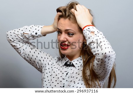 Portrait of a frustrated young screaming woman pulling her hair on gray background