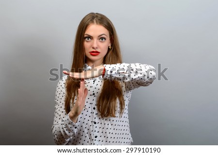 Young woman with a serious face showing time out hand gesture, isolated on grey wall background.