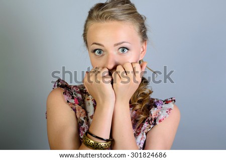 Woman afraid covering her mouth with his hands. On a gray background.
