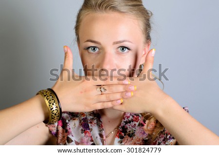 Woman covering her mouth with his hands. On a gray background.