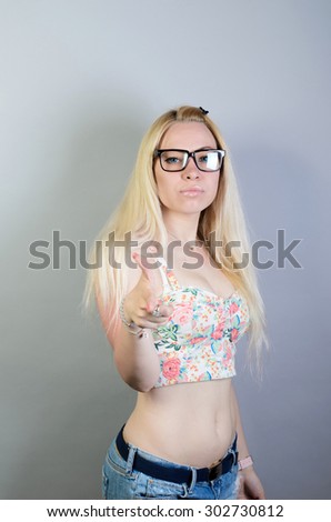 Vivacious attractive blond middle-aged woman pointing at the camera with a beaming playful smile, blackboard background with copyspace