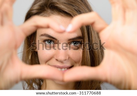 Romantic woman making a heart gesture with her hands framing her laughing eyes as she shows her feelings of love and affection