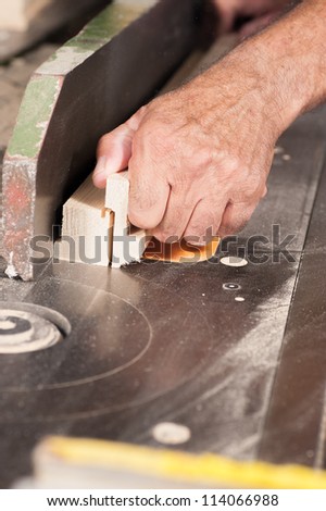 Carpenter hands holding a plank on a table saw