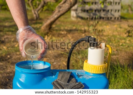 Hand with plastic glove filling pesticide into a garden sprayer