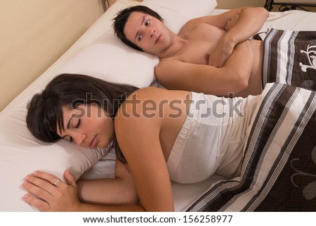 Frustrated guy  in bed looking at his sleeping  partner