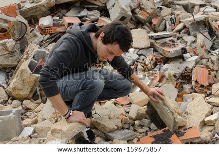Lonely guy  rummaging  in lots of debris from a pulled down house