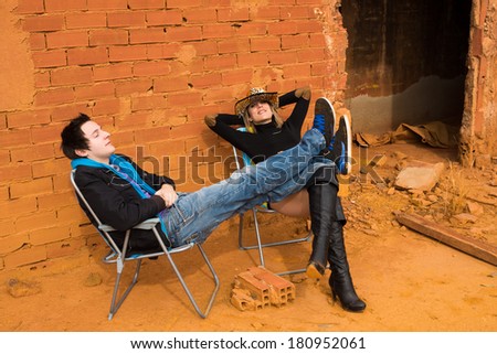 hard times, couple sunbathing among industrial ruins, a concept
