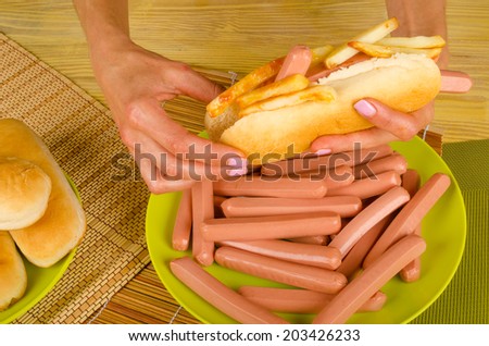 Female hands holding hot dog stuffed with a lot of sausages and french fries, an unhealthy food concept