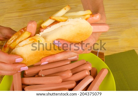 Female hands holding hot dog stuffed with a lot of sausages and french fries, an unhealthy food concept