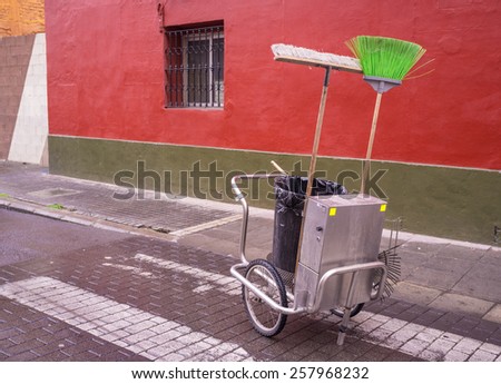 Cleaning trolley with brooms and bin on a cobblestone street
