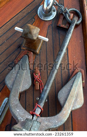 Brass anchor lashed to a cleat on a vintage, teak sailboat deck.