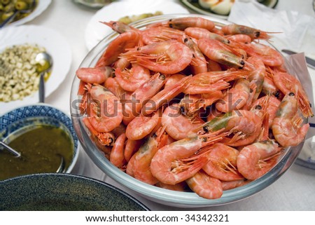 A bowl of large, cooked, unpeeled (head on) shrimp with other dishes visible on table with white table cloth.