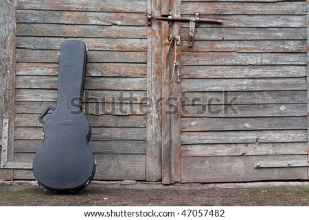 The guitar case rest on a gate.