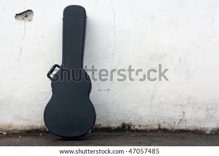 The guitar case rest on a wall.