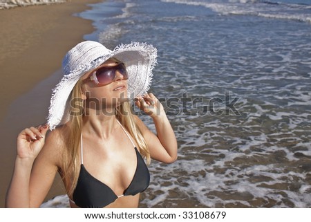 Young smiling blond caucasian white woman wearing black bikini, hat and sunglasses.