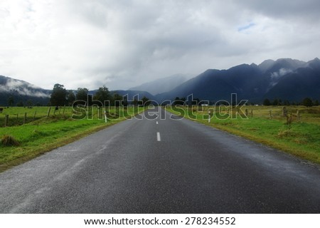 A long road towards mountains with gloomy sky