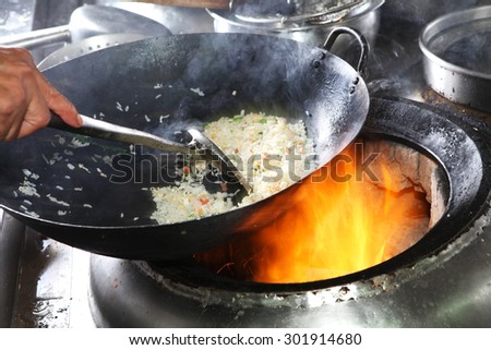 Chef cooking fried rice with flame in a frying pan on a kitchen stove, Chinese style