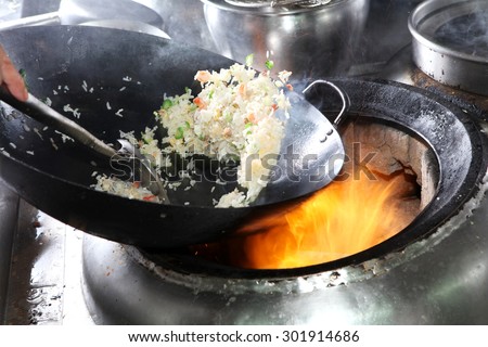 Chef cooking fried rice with flame in a frying pan on a kitchen stove, Chinese style